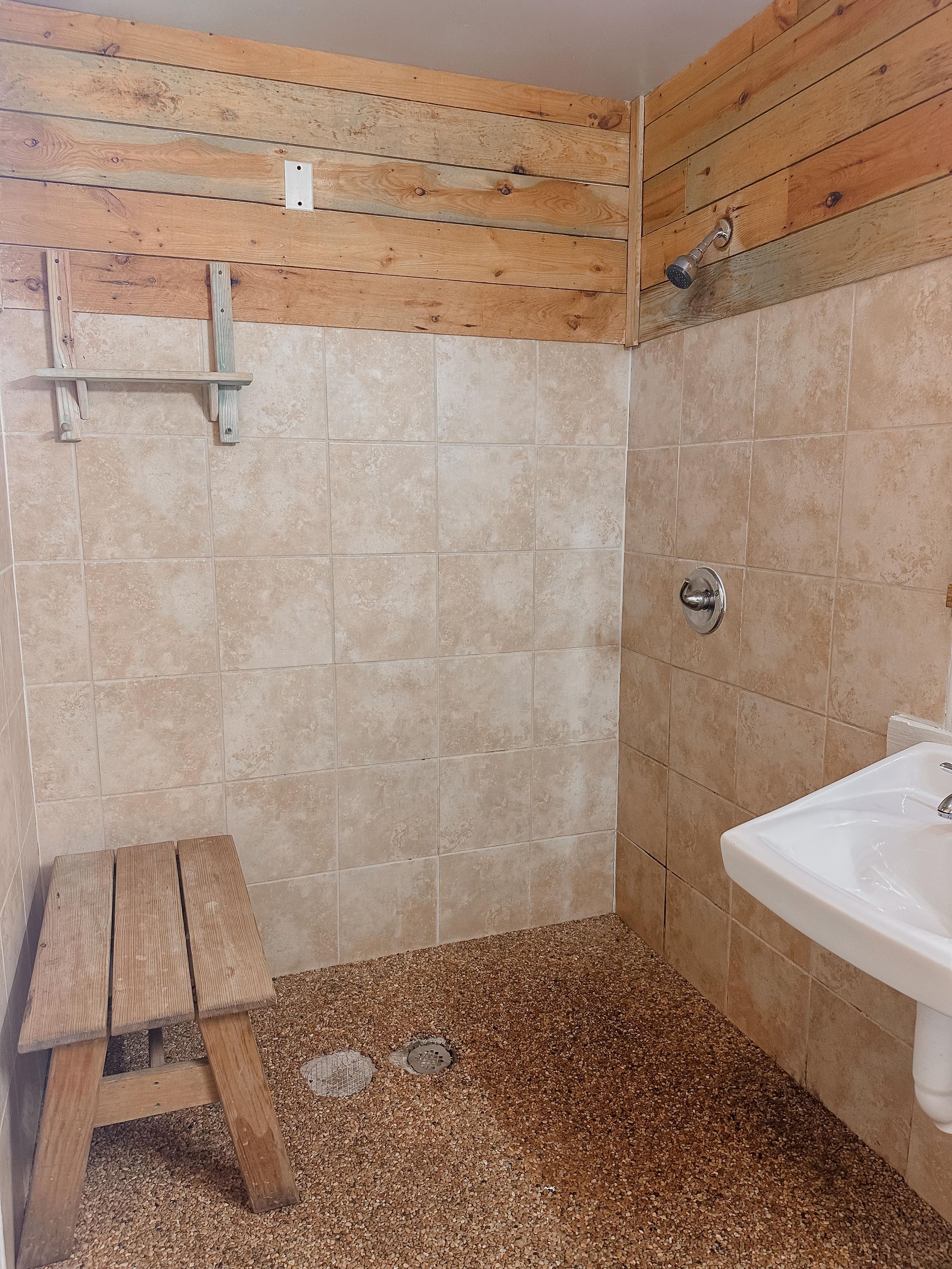 A bathroom with wooden paneling, a tiled floor, a sink, and a shower.