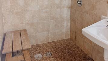 A bathroom with wooden paneling, a tiled floor, a sink, and a shower.
