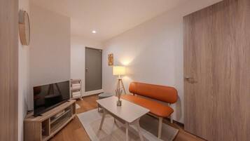 A compact living space with a television, a bench, a small table, and a lamp.