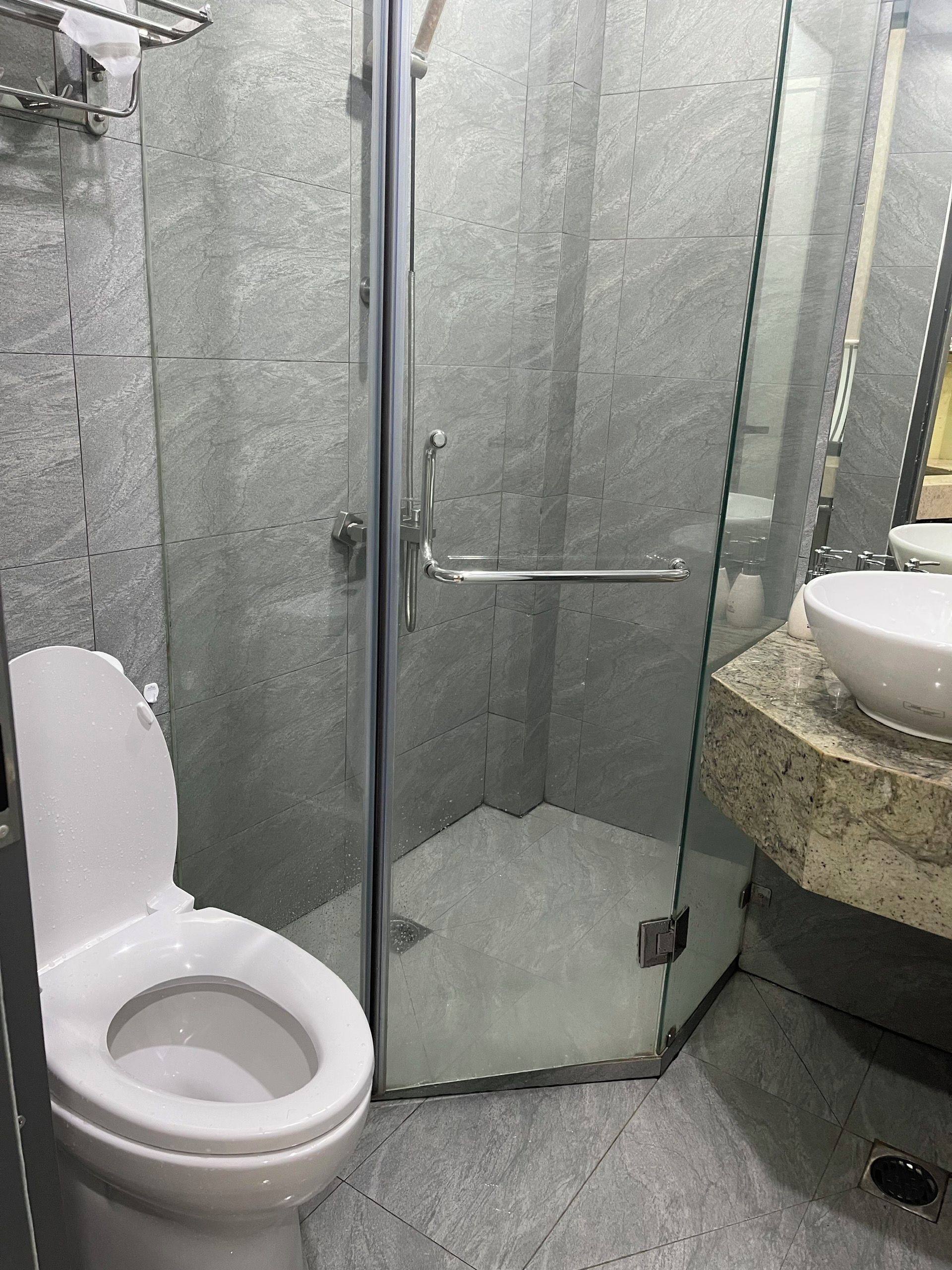 A bathroom with a glass-enclosed shower, a toilet, and a sink with a marble countertop.