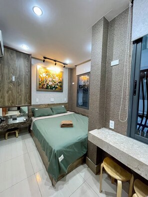 Quarto de hotel com cama, escrivaninha, cadeira, janela e um quadro na parede.