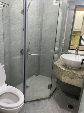 Uma casa de banho moderna com cabine de duche em vidro, sanita branca e lavatório com bancada em mármore.
