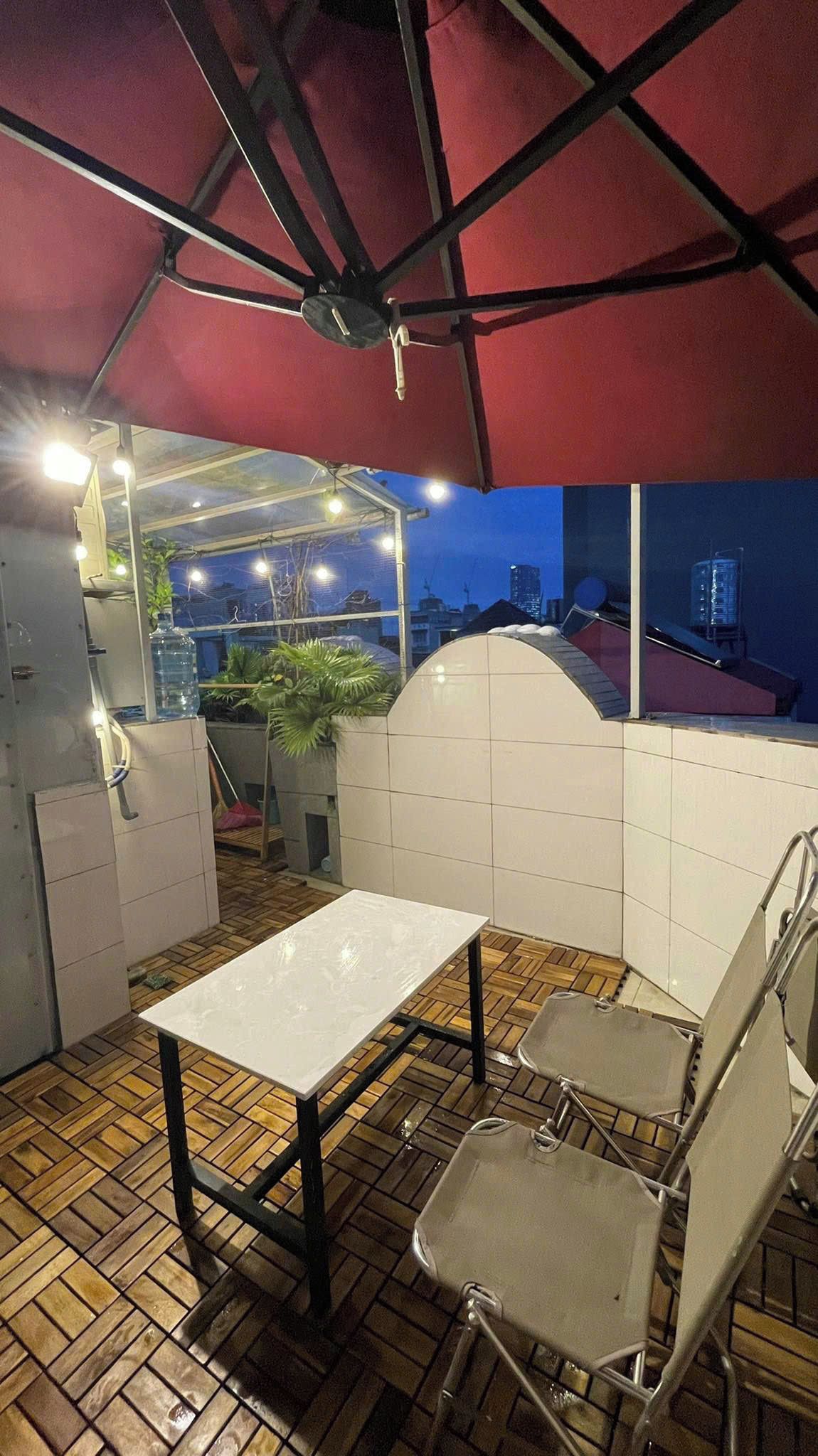 An outdoor patio area with a table and chairs, a red canopy, and a view of the cityscape.