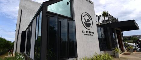 A modern boutique hotel with a glass facade, a logo with a leaf and a bird, and a sign that reads 'CHARTAME Boutique Hotel.'