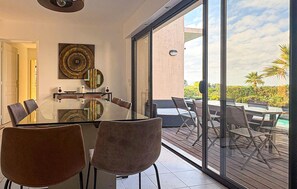 Ein moderner Essbereich mit einem Glastisch, Stühlen, einer Wanddekoration und Blick ins Freie.