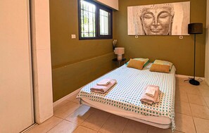 Un dormitorio con cama, almohadas, mesita de noche, lámpara y un cuadro en la pared.