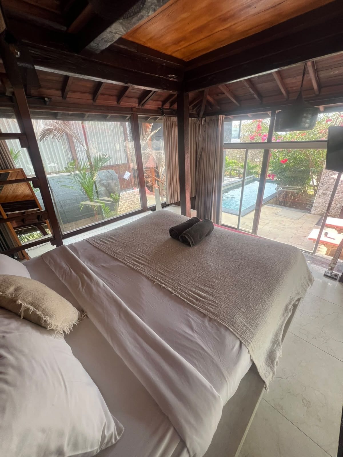 Une chambre avec un grand lit, une vue sur une piscine et un plafond en bois.
