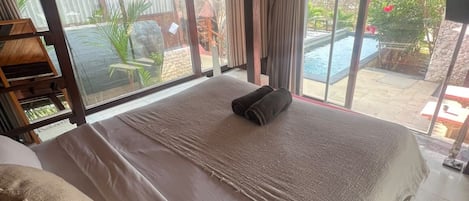 Une chambre avec un grand lit, une vue sur une piscine et un plafond en bois.