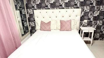 A bed with a white headboard and two pillows, a bedside table, and a mirror on the wall.