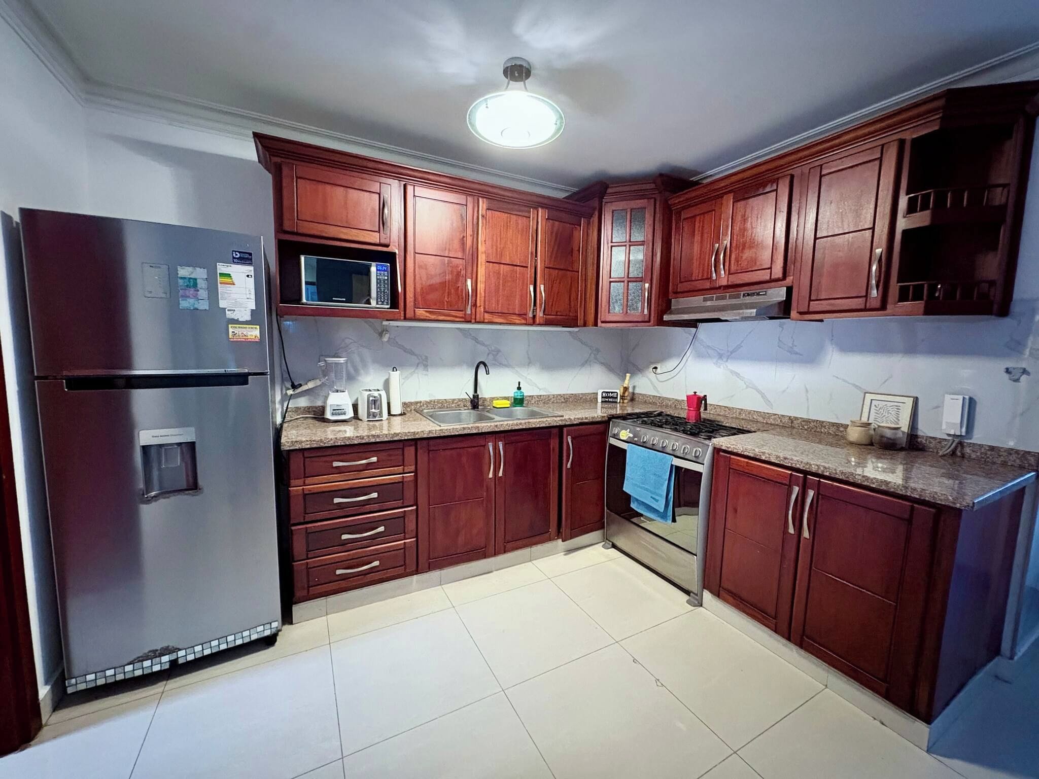 Una cocina con armarios de madera, un refrigerador, un microondas, una estufa y un lavamanos.