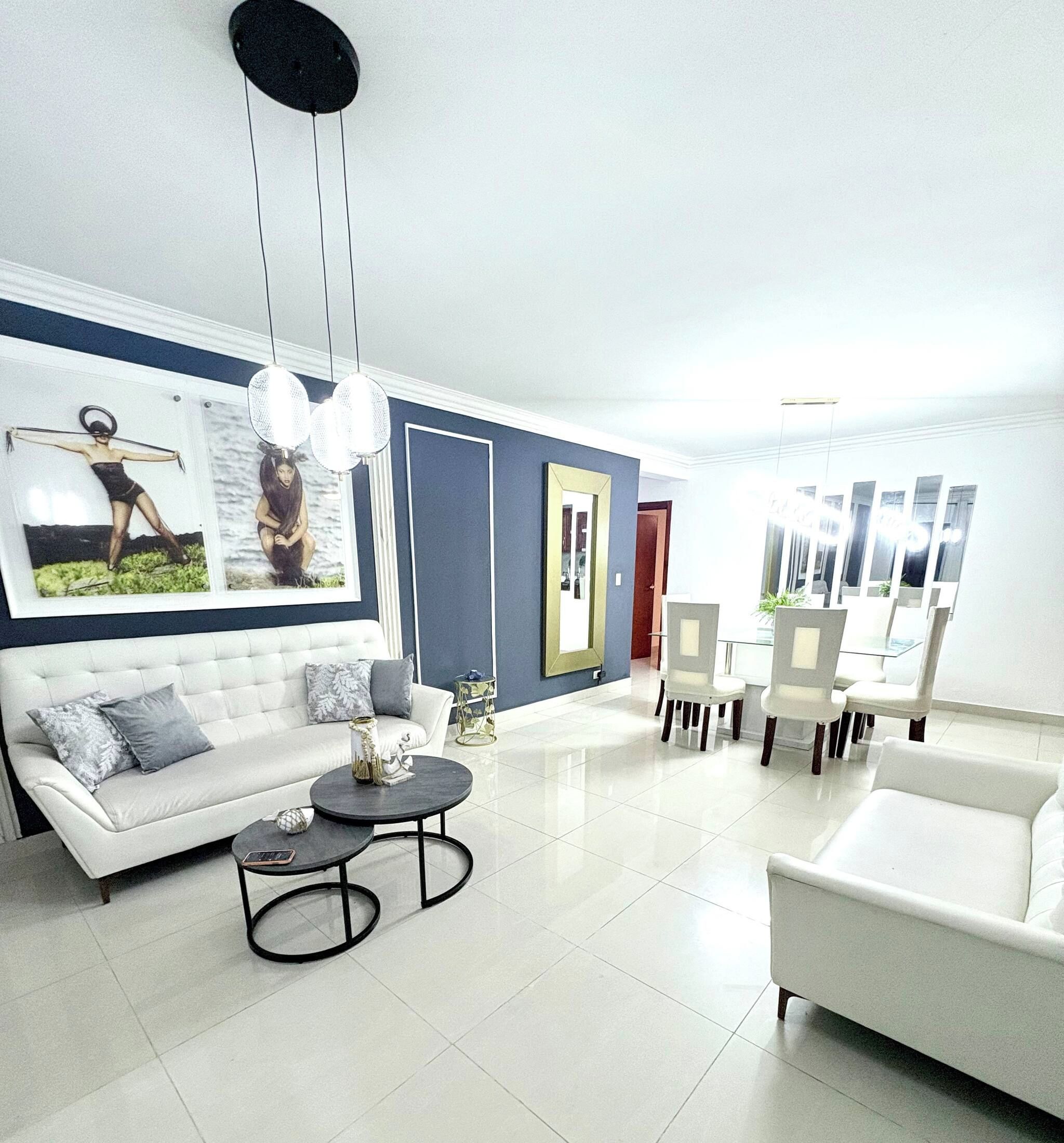 A modern living room with a white sofa, a round coffee table, and a dining area with chairs and a table.