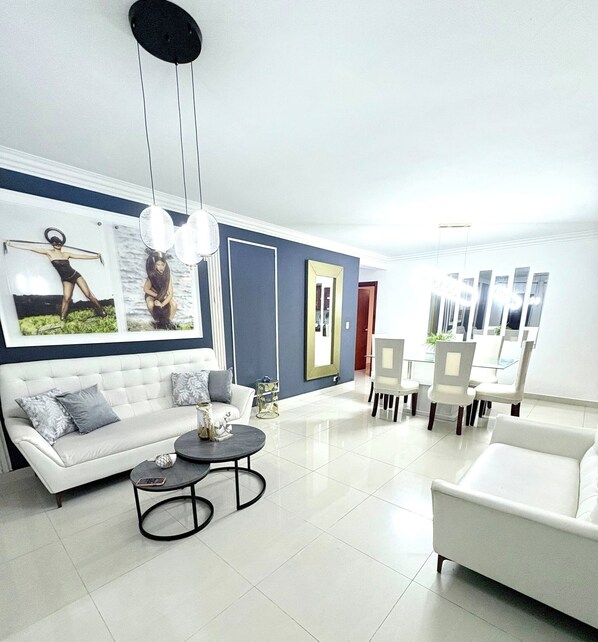 Uma sala de estar moderna com um sofá branco, uma mesa de centro redonda e uma área de jantar com cadeiras e uma mesa.