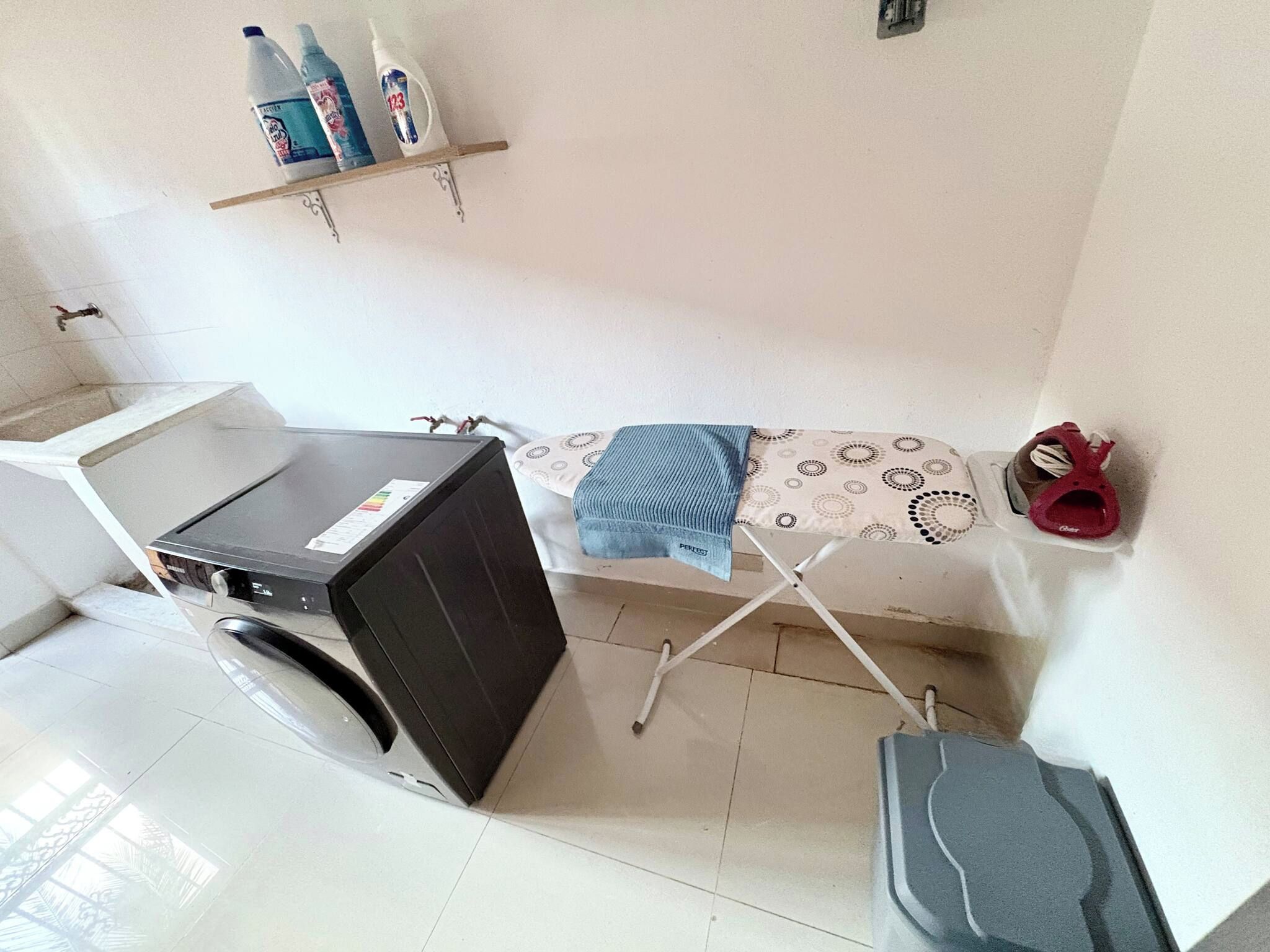 A compact laundry area with a washing machine, a drying rack, and a pair of shoes.