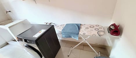 Un espacio de lavandería reducido con lavadora, tendedero y un par de zapatos.