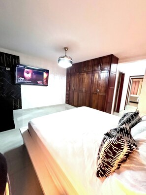 A bedroom with a bed, a television mounted on the wall, and wooden cabinets. - Spacious 3BR Near Airport & Ocean (Santo Domingo Este)