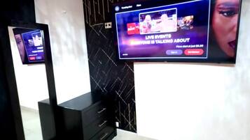 A modern room with a large flat-screen TV mounted on the wall, a black console table, and a tiled floor.