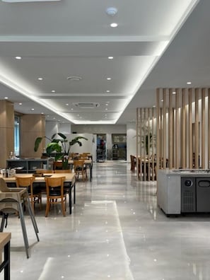 Um interior moderno com área de jantar, mesas, cadeiras e cozinha.