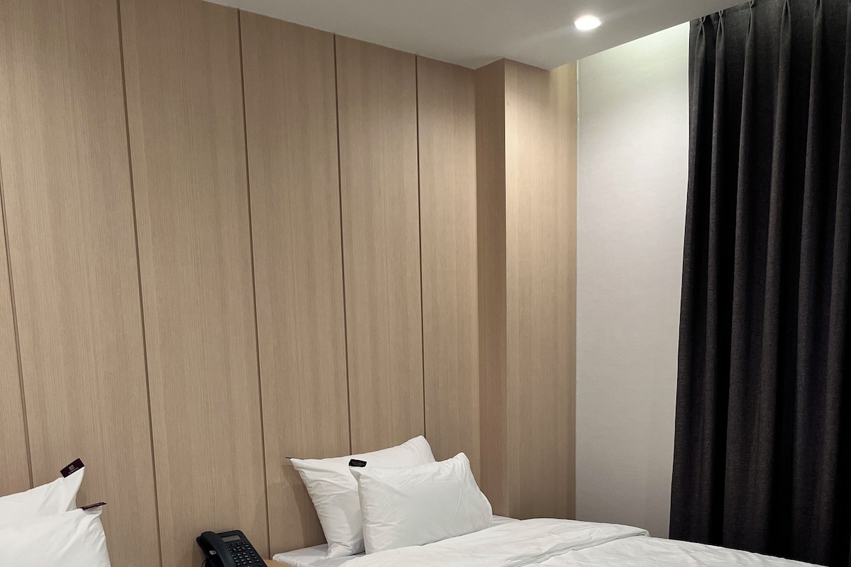 Quarto de hotel com duas camas, telefone ao lado da cama e parede revestida de madeira.