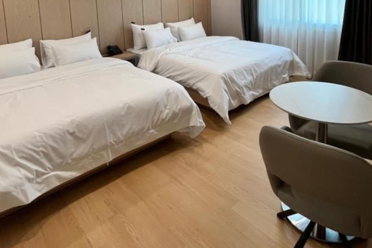Quarto de hotel com duas camas, uma mesa redonda e uma cadeira.