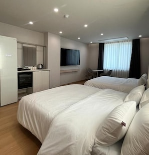 Quarto de hotel com cama, escrivaninha, televisão e janela com cortinas.