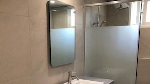 Ein modernes Badezimmer mit einer Duschkabine aus Glas, einem Waschbecken mit dunkler Arbeitsplatte und einem Spiegel darüber.
