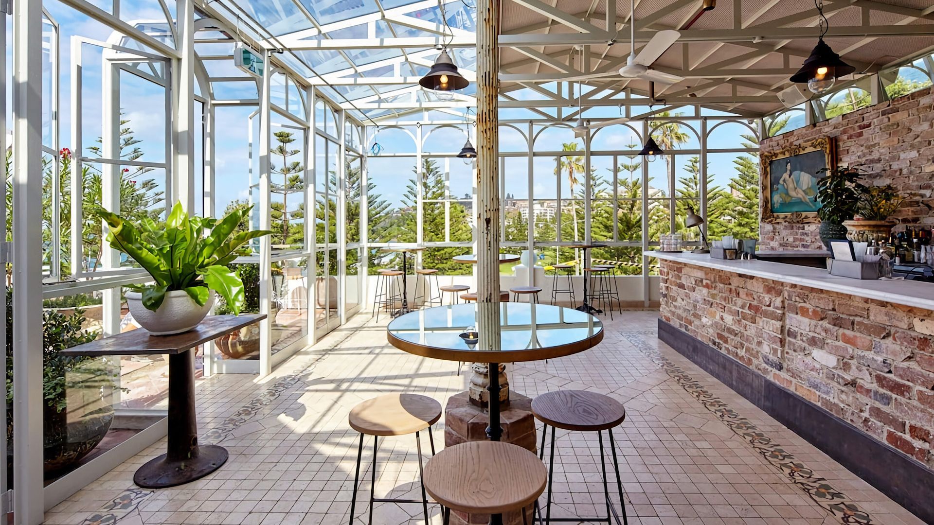 A spacious conservatory with a glass ceiling, a central round table, and a brick bar area.
