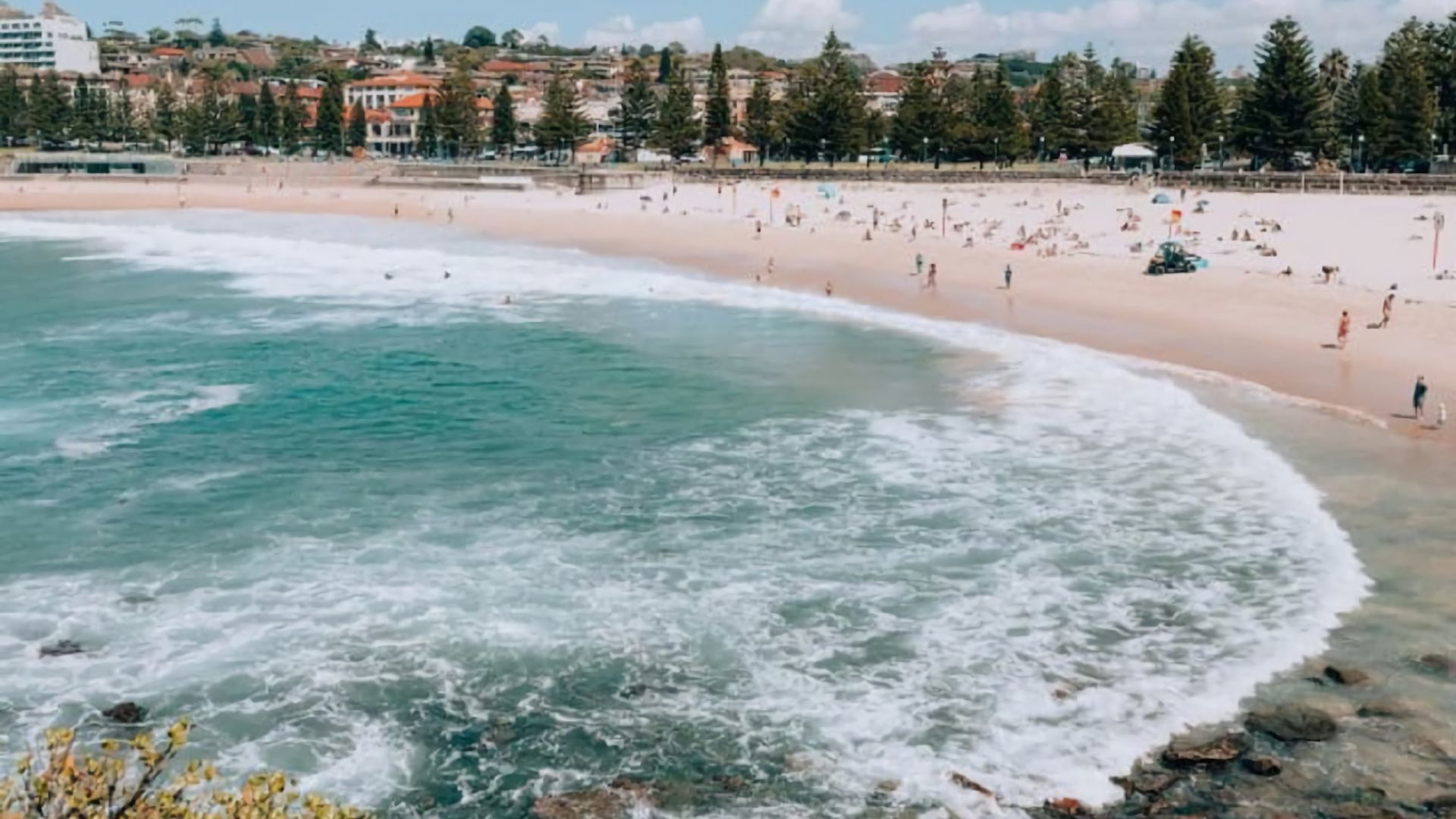 A beach with waves, people, and buildings in the background.