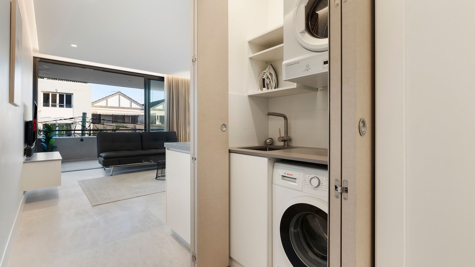 A modern apartment with a laundry area, a sofa, and a view of the outside.