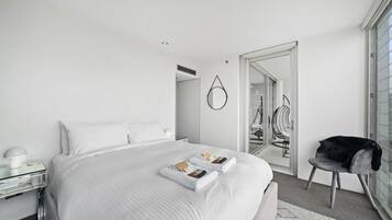 A modern bedroom with a large bed, a chair, a mirror, and a wardrobe.
