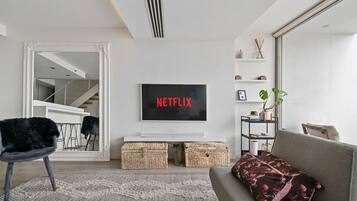 A living room with a flat-screen TV mounted on the wall, a sofa, a chair, and a decorative plant.
