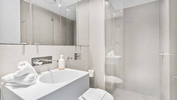 A modern bathroom with a large white sink, a mirror, and a glass-enclosed shower area.