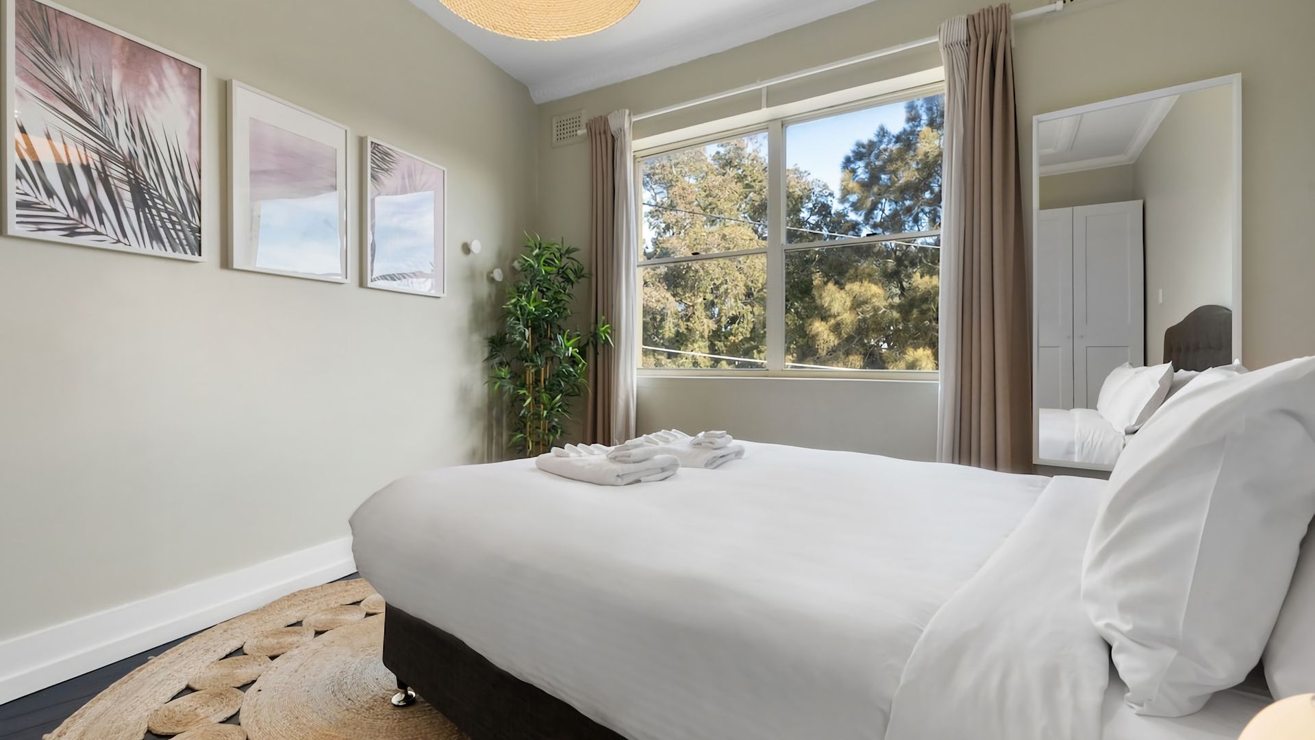 A hotel room with a large bed, a window with curtains, and framed artwork on the wall.