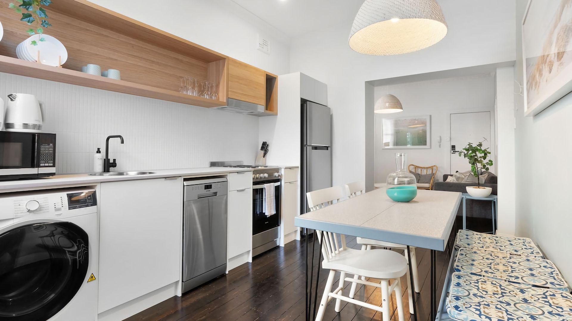 A modern kitchen with a dishwasher, oven, and microwave. There is a dining table with chairs and a bench.