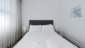 A hotel room with a bed, two bedside tables, a remote control, and a painting on the wall. - Sleek 1BR Apartment w Skylight near Coogee Beach (Coogee)