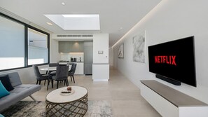 A modern living room with a flat-screen TV displaying the Netflix logo, a sofa, a coffee table, and a dining area in the background. - Sleek 1BR Apartment w Skylight near Coogee Beach (Coogee)