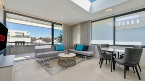 A modern living room with a sofa, coffee table, and chairs, large windows, and a view of the city. - Sleek 1BR Apartment w Skylight near Coogee Beach (Coogee)