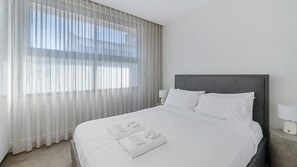 A hotel room with a bed, a nightstand, a lamp, and sheer curtains. - Sleek 1BR Apartment w Skylight near Coogee Beach (Coogee)
