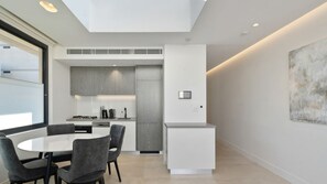 A modern kitchen with a dining area, featuring a central island, grey cabinetry, and a minimalist design. - Sleek 1BR Apartment w Skylight near Coogee Beach (Coogee)