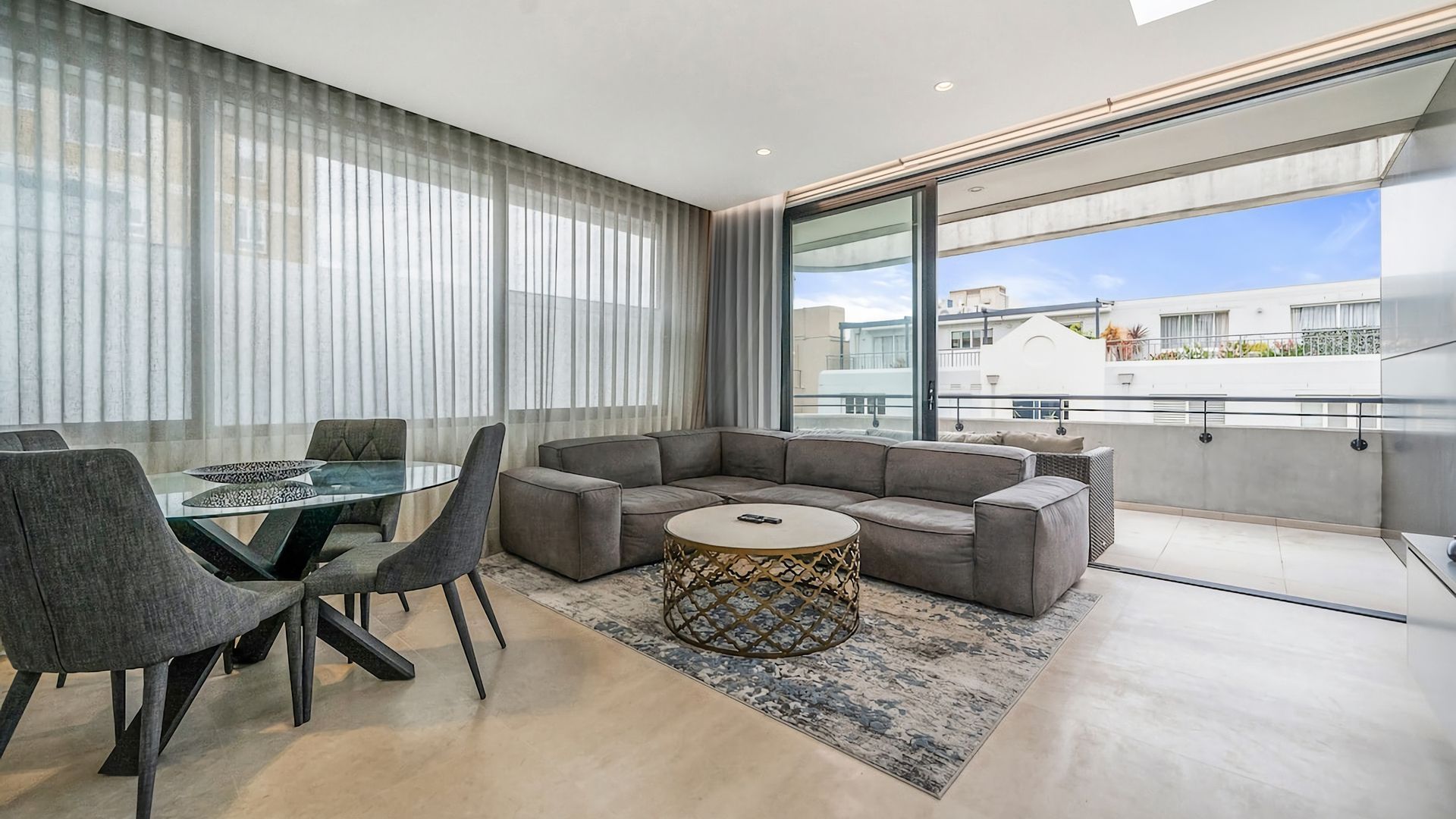 Un salon moderne avec une table à manger en verre, des canapés gris et un tapis à motifs.