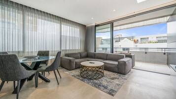 Un salon moderne avec une table à manger en verre, des canapés gris et un tapis à motifs.