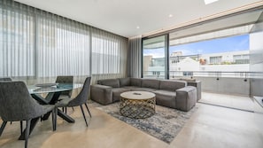 Un salon moderne avec une table à manger en verre, des canapés gris et un tapis à motifs.