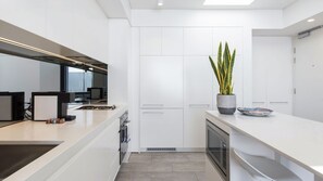 A modern kitchen with white cabinetry, a central island, a built-in oven, and a potted plant. - Top Floor Bondi Retreat Near Beach, Cafes & Dining (Bondi Beach)
