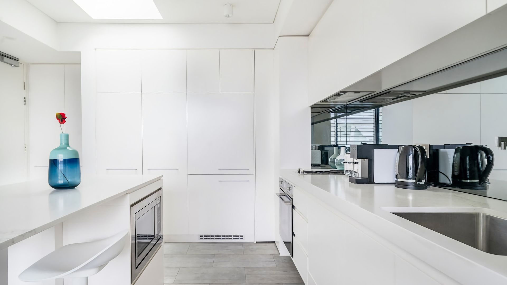 A modern kitchen with white cabinetry, a built-in oven, a coffee machine, and a sink.