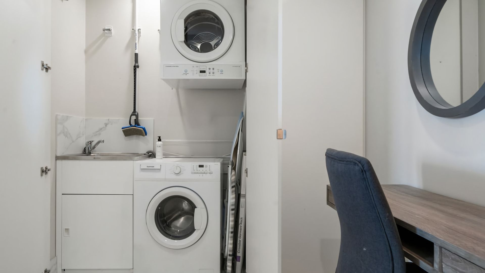 A compact laundry room with two front-loading washing machines, a sink, and a mirror.