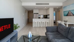 A modern living room with a flat-screen TV, a glass coffee table, and a grey sofa. - Bondi Junction Living with Views & Double Parking (New South Wales)
