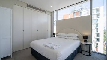 Un dormitorio con una cama, una mesita de noche, una lámpara, una ventana y un armario.