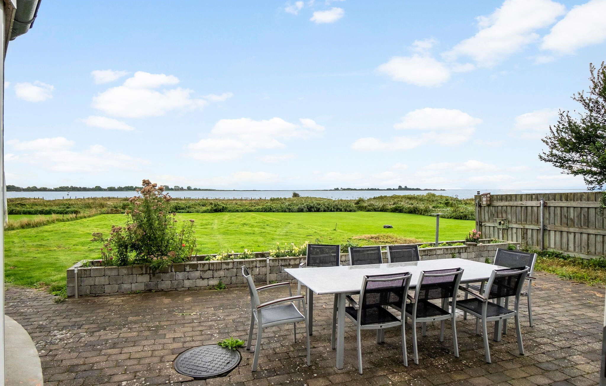 An outdoor patio with a table and chairs, a view of a grassy field, and a wooden fence.