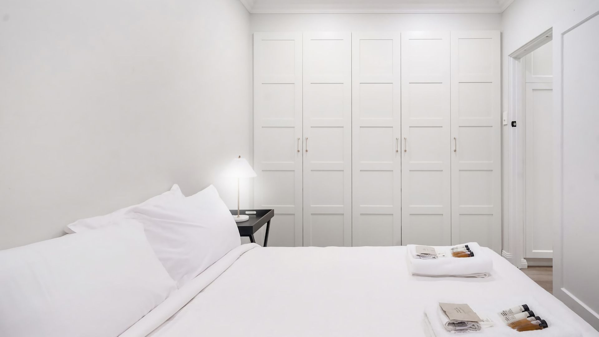 A hotel room with a bed, a nightstand, a lamp, and a wardrobe.