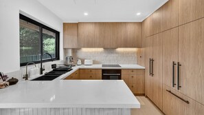 A modern kitchen with a large island, wooden cabinets, and a window providing a view of greenery. - Spacious North Bondi Apt w Balcony near beach (Bondi Beach)