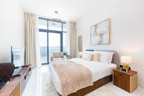 A modern bedroom with a large bed, a desk, and a view of the city. - Bloomfields Studio the Gate Masdar (Abu Dhabi)